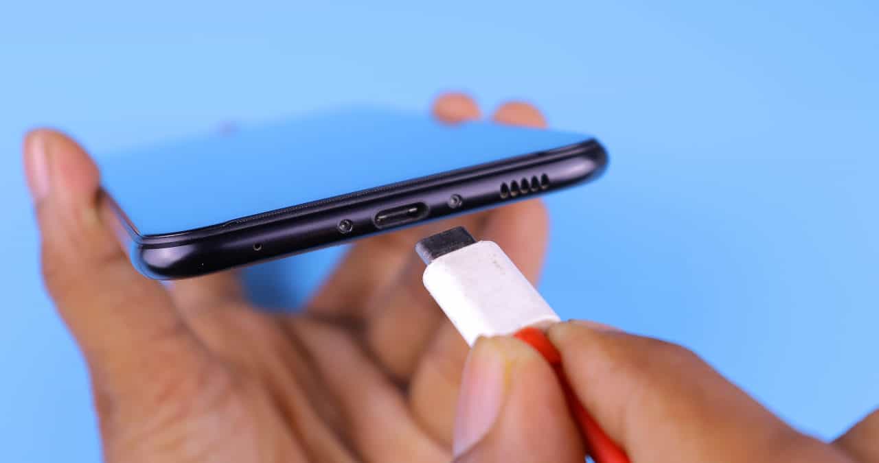 person holding a phone and putting it on the charge with a white and red power cable